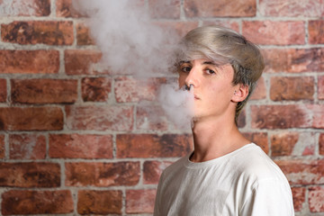 Vaper Smoke outdoor electronic cigarette near the brick wall. Young man smoking big cloud of steam