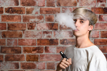 Vaper Smoke outdoor electronic cigarette near the brick wall. Young man smoking big cloud of steam