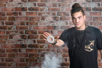 Vaper Smoke outdoor electronic cigarette near the brick wall. Young man smoking big cloud of steam