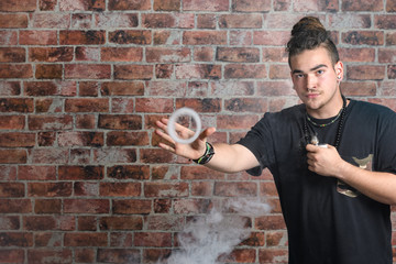 Vaper Smoke outdoor electronic cigarette near the brick wall. Young man smoking big cloud of steam