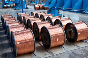 Several rows of new finished coils with copper wire in the production shop. Copper wire is wound on metal coils or drums. Modern line of automatic production of electric cable and wire.