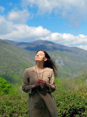 Brunette girl in beige linen dress standing on background of green caucasus mountains in Sochi, Russia. Freedom ecology lifestyle concept.