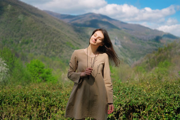 Brunette girl in beige linen dress standing on background of green caucasus mountains in Sochi, Russia. Freedom ecology lifestyle concept.