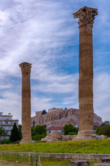 Athens, Attica / Greece. The Temple of Olympian Zeus also known as the Olympieion or Columns of the Olympian Zeus. Between the ancient columns the Acropolis of Athens with the Parthenon. Cloudy sky