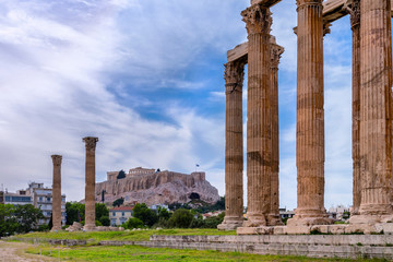 Athens, Attica / Greece. The Temple of Olympian Zeus also known as the Olympieion or Columns of the Olympian Zeus. Between the ancient columns the Acropolis of Athens with the Parthenon. Cloudy sky