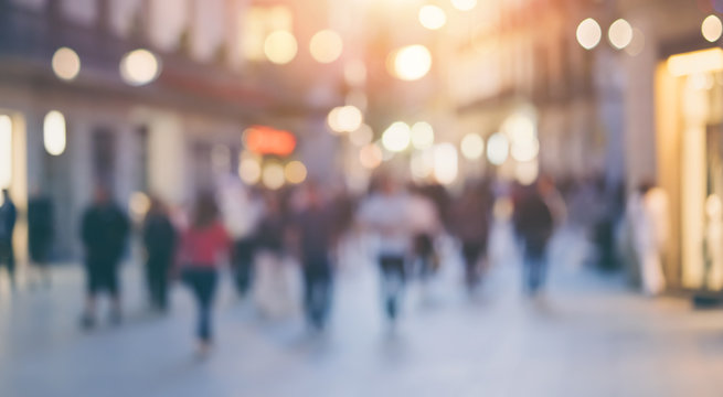 Group of unrecognizable anonymous people in bokeh walking on a street in the evening. Defocused image