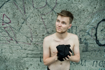 Obraz na płótnie Canvas A young man with red hair and a beard removing a T-shirt on the background of a concrete wall with graffiti.