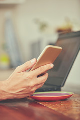Modern bearded man using cellphone and drinking coffee with laptop.