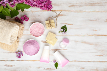 Obraz na płótnie Canvas Spa and bath cosmetics with lilac flowers. Bath salt, soap, cream, oil, serum and towel rolls on wooden rustic background. Organic natural cosmetics. Fresh care of body. Beauty and relax healthcare