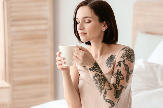 Beautiful tattooed woman drinking coffee in morning at home