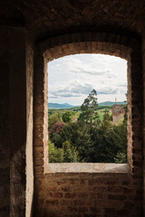 view through old medieval window of landscape in a sunny day with forest mountains and clouds
