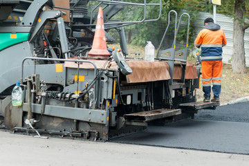 Fototapeta na wymiar Asphalt paver machine or paver finisher places a layer of fresh hot asphalt. Road construction working. Road renewal process. Close-up view, selective focus