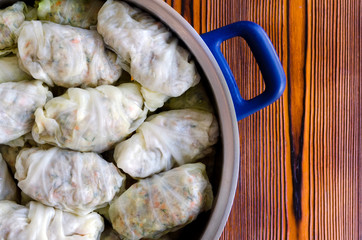 Cabbage Rolls or Dolma. Stuffed cabbage leaves with minced meat, rice, vegetables and herbs in casserole. Isolated on rustic wooden table, copy space for your text. Top view. Sarma, golubtsy, golabki.