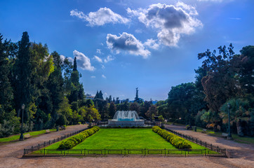 Athens, Attica / Greece. The garden with the marble fountain in front of the Zappeion Hall neo-classical building in the National Garden near Syntagma Square. Sunny day, cloudy sky, nobody