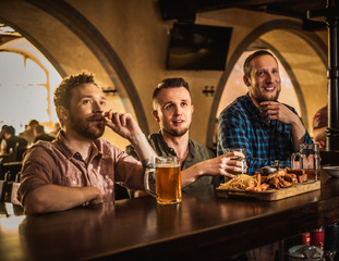 Friends drinking draft beer and watching tv in a pub