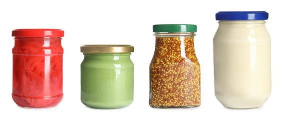 Set of glass jars with different delicious sauces on white background