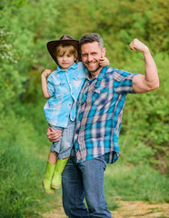 Fototapeta premium strong father and son in cowboy hat on ranch. kid in rubber boots. happy man dad in forest. human and nature. family day. happy earth day. Eco farm. small boy help father in farming. strong bonds