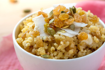 Cooked bulgur with raisins, seeds and coconut in a white bowl on a wooden table. Sweet bulgur porridge close up, Turkish cuisine.