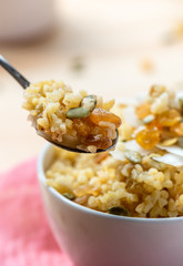 Cooked bulgur with raisins, seeds and coconut in a white bowl and spoon. Sweet bulgur porridge close up, Turkish cuisine.