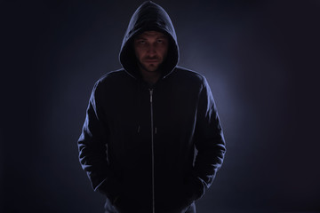 Mysterious man in hoodie on dark background. Dangerous criminal