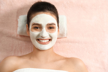 Beautiful woman with white mask on face relaxing in spa salon, top view