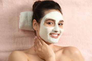 Beautiful woman with white mask on face relaxing in spa salon, top view