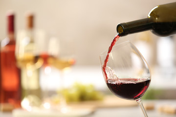 Pouring red wine from bottle into glass on blurred background. Space for text