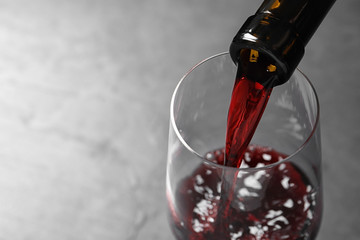 Pouring red wine from bottle into glass on grey background, closeup. Space for text