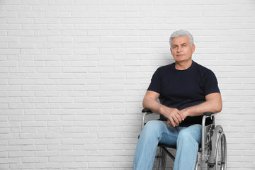 Fototapeta na wymiar Senior man in wheelchair near brick wall indoors. Space for text