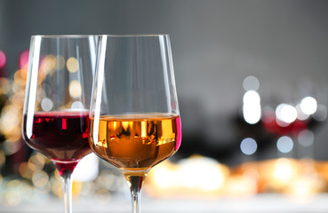Glasses with different wines against defocused lights, closeup. Space for text