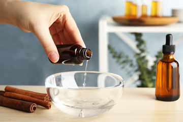 Woman adding cinnamon essential oil from bottle into bowl of water on table indoors, closeup