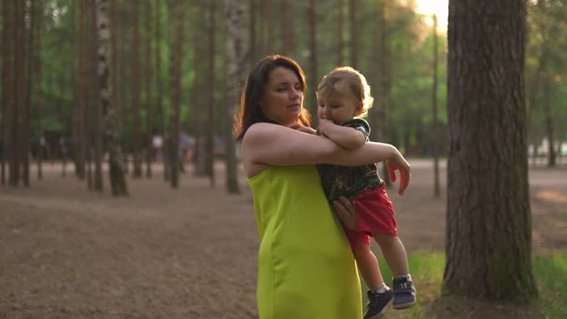 Mother walking playing baby child boy in forest wood - Young mom in green dress and her baby in a green park having fun - Happy smiling people