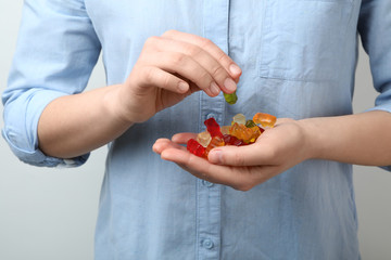 Woman holding colorful jelly bears on light background, closeup