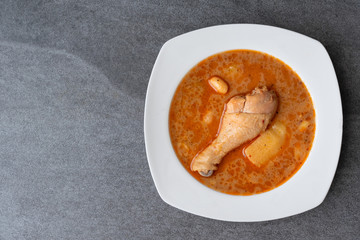 Massaman curry with chicken drumstick or leg and potato in white dish on table.