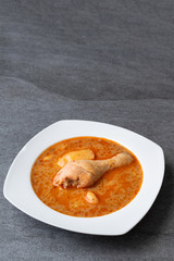 Massaman curry with chicken drumstick or leg and potato in white dish on table.