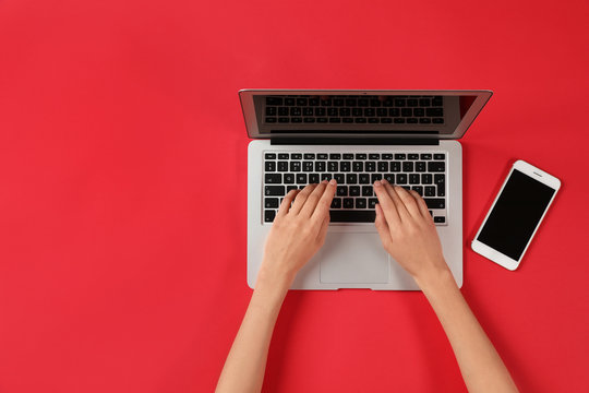 Woman using modern laptop at color table, top view