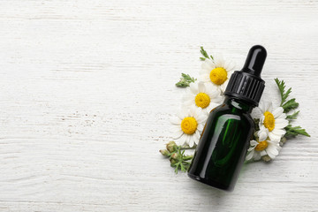 Flat lay composition with bottle of chamomile essential oil and space for text on white wooden background