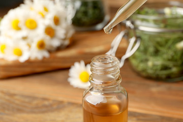 Pipette with essential oil over bottle on blurred background, closeup. Space for text