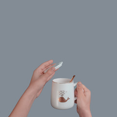 White cup with a spoon in the hand of a teenager, on an isolated gray background