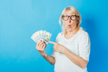 Old lady with glasses holds money in her hands against a blue background. Concept of wealth,...