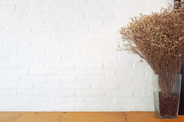 white brick wall background with dried flowers on wooden table