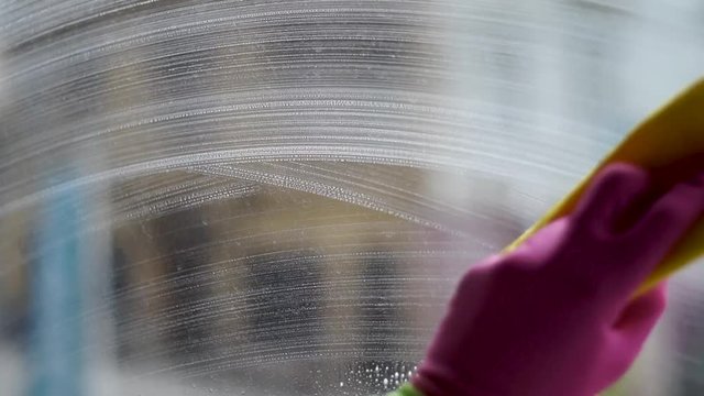 Spraying and washing windows with a yellow rug and gloves close up