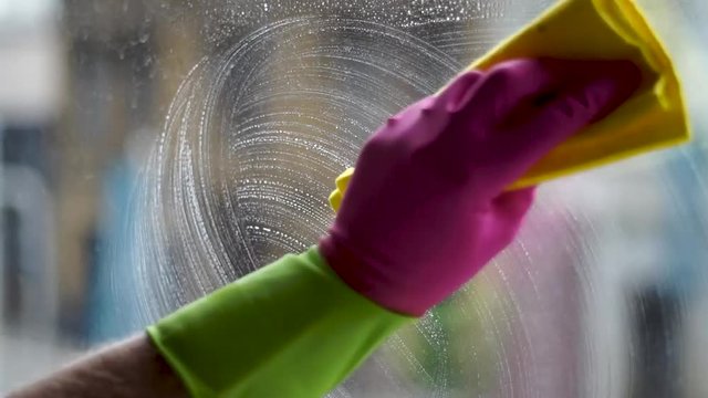 Spraying and washing windows with a yellow rug and gloves close up