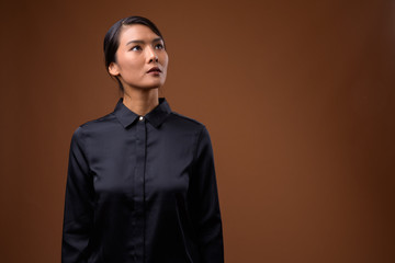 Studio shot of beautiful Asian businesswoman against brown backg