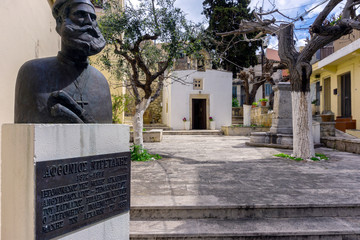Archanes, Crete Island / Greece. The "Holy Cross Chapel" in Archanes town. Stone carved fountain at the courtyard, statue of a cretan revolution's hero against the Ottoman empire