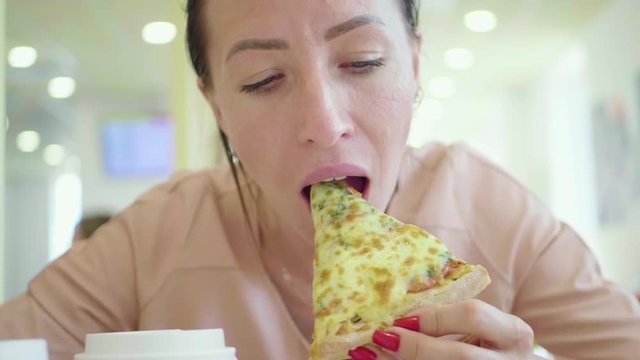 A young woman is eating a piece of pizza. Charming happy girl laugh and biting off big slice of fresh made pizza. International food concept. Close up.
