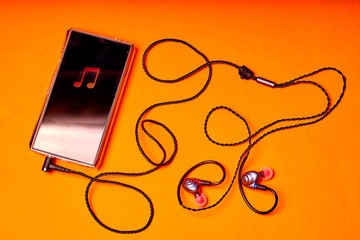 Portable music player on orange background with earphones and wire