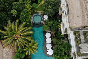 Aerial view of luxury hotel with straw roof villas and pools in tropical jungle and palm trees. Luxurious villa, pavilion in forest, Ubud, Bali