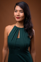 Studio shot of beautiful Asian businesswoman against brown backg