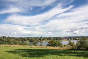 View of the lake from the hill. Green beautiful park with trees on a sunny day. A small village on a lake in the background.